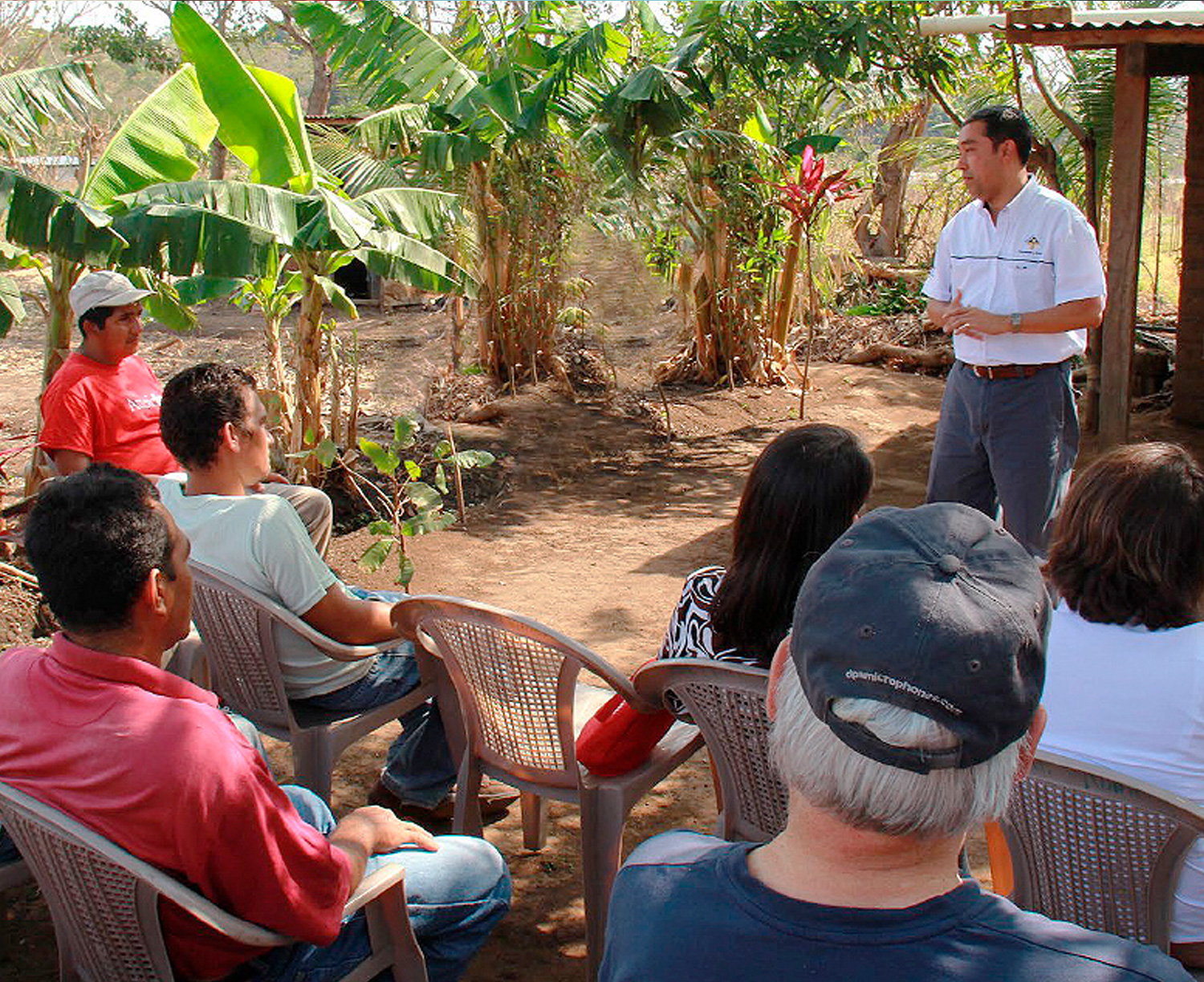 Un hombre latinoamericano de pie da una charla sobre la lectura del medio ambiente a participantes sentados en una granja.