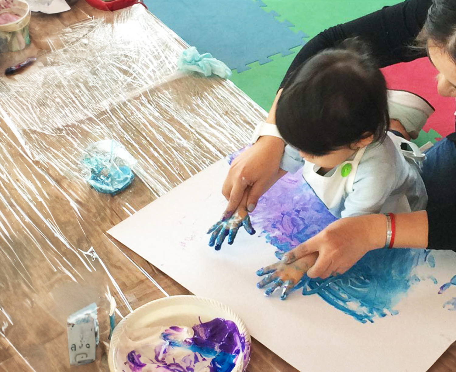 Uma criança pinta com as mãos com tinta azul em um pedaço de papelão.